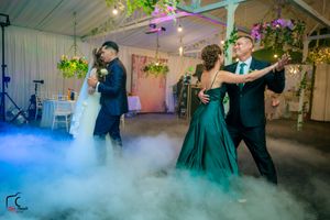Guests dance on a misty dancefloor with emerald green and blue lighting effects at a wedding celebration.