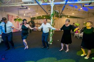 Group dance formation on a blue-lit floor with hanging plants and party decorations.