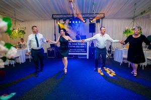 Group of dancers performing synchronized moves on a blue-lit dance floor at a celebration.