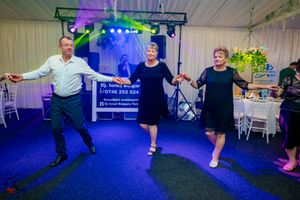 Three people dancing energetically on a blue dance floor with colorful lighting and decorations at an indoor event.