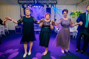 Celebration guests dancing in formation under purple and blue theatrical lighting at an indoor venue.