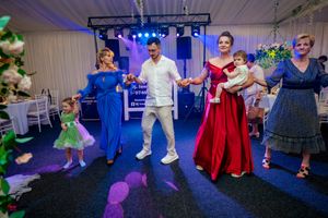 Party guests performing coordinated dance moves under vibrant blue and green stage lighting.