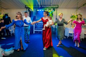 Group of party guests dancing in a line formation under colorful stage lighting at an indoor event.