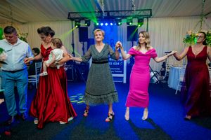 Line of dancers in formal dresses performing traditional moves at indoor celebration event.