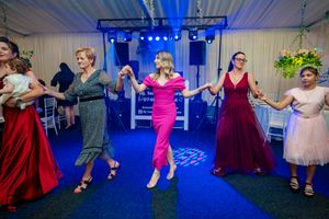 Group of dancers in colorful dresses performing traditional dance moves on blue-lit dance floor.