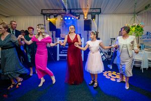 Festive group dance with participants in formal attire on blue-carpeted floor with stage lighting.