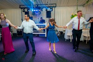 Group of guests dancing together in a line formation at a wedding reception with purple lighting.