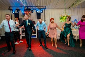 Wedding guests dancing in a line on a red-lit dance floor at a reception party.