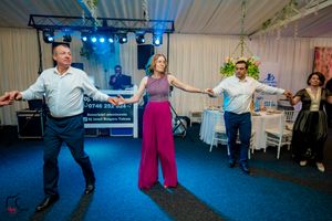 Event participants dancing in formation on a blue carpet with decorative lighting and white wall backdrop.