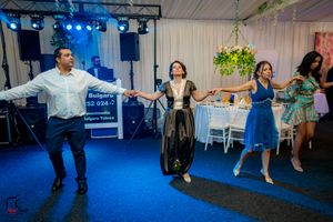 Dancers spread across a blue-lit dance floor performing synchronized movements at an indoor celebration.
