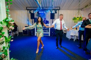 Celebratory dance moves being performed on a blue dance floor under stage lighting at an indoor event.