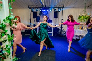 Party guests dance in formation during an event with blue lighting and white drapes in the background.