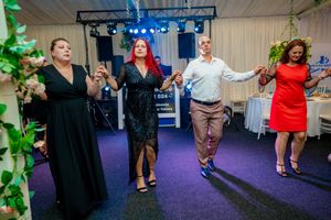 People dancing in pairs on a purple carpet under blue stage lighting at an indoor venue.
