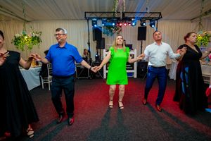 People dancing in a line at an indoor event with blue lighting and decorative elements.