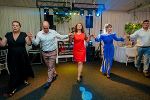 People dancing in a line at an indoor reception with stage lighting and white tent walls.