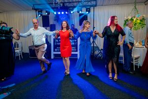 Group of guests dancing in colorful dresses under blue lighting at a wedding reception.