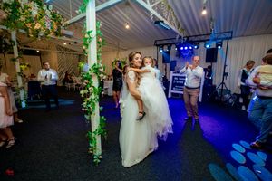 A couple dances together at a wedding reception decorated with green vine accents and blue lighting.