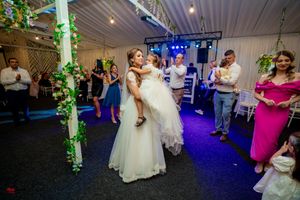 A couple shares their first dance at a wedding reception with purple lighting and floral decor.