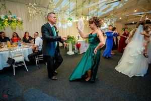 Wedding guests dancing energetically in formal attire under decorative lighting.