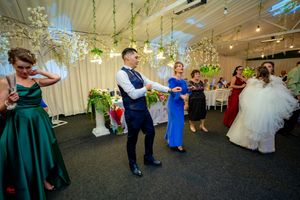 Wedding guests dancing in formal attire under elegant hanging lights and greenery.