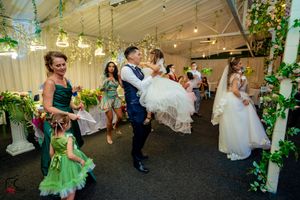 Wedding celebration with guests dancing under decorative lights and floral arrangements.