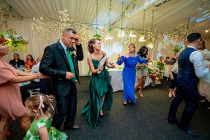 Wedding reception dance floor with guests in formal attire under hanging floral decorations.
