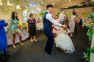 Couples dancing at a wedding reception decorated with hanging lights and greenery.