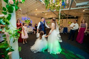 Wedding couple dances under green-lit decorative vines and fairy lights at their reception.