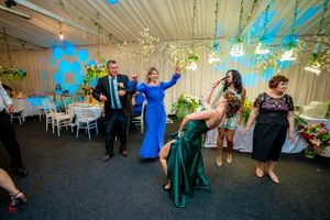Guests dancing energetically at a wedding reception decorated with blue lighting and hanging greenery.