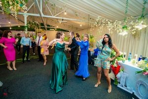 Wedding guests in colorful dresses dance and celebrate in a decorated reception hall.