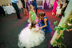 Wedding party dances in a decorated reception venue with colorful lighting and floral accents.