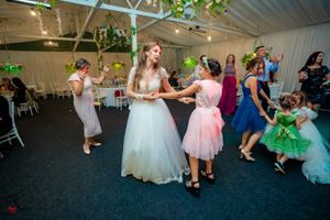 Wedding reception guests dance and celebrate on a dark carpeted floor under decorative lighting.