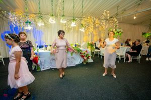 Wedding reception venue decorated with hanging lights and white decor as guests dance.