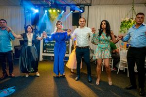 People dancing in a line at an indoor celebration with blue and green lighting effects.