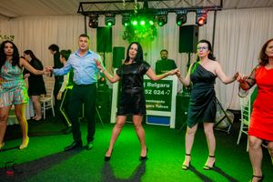 Dance floor filled with people performing synchronized moves under green lighting.