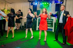 Party guests dancing in a line formation under green and blue lighting effects.