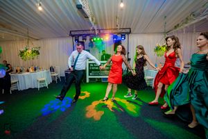 Wedding guests dancing at a reception with colorful lighting and white drapes in the background.