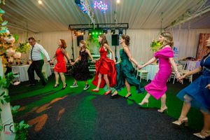 Wedding guests performing a choreographed line dance on a green-lit dance floor.