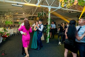 Guests dancing at an indoor celebration with greenery decorations and white curtained walls.