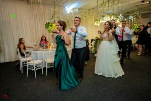 Wedding guests dancing in formal attire at a reception decorated with white drapes and greenery.
