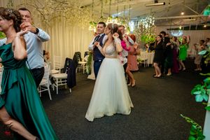 Wedding reception dance party in a modern venue with hanging floral decorations and white drapes.