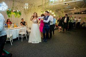 Wedding celebration with dancing couples in an indoor venue decorated with hanging greenery.