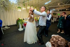 Couples dancing and celebrating at an indoor reception decorated with hanging greenery and white drapes.