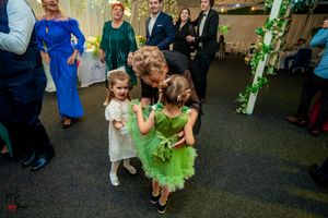 Young children in formal attire dance together at an indoor wedding reception with decorative greenery.