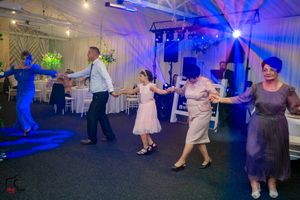 Indoor celebration with dancers moving across the floor under bright blue atmospheric lighting.