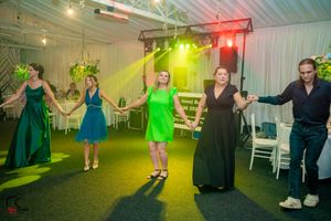 Wedding celebration with guests dancing in a venue decorated with white walls and colorful lighting effects.