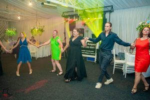 Reception guests dancing in formation under bright multicolored lighting at an indoor venue.