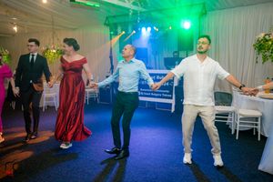 Guests performing coordinated dance moves under vibrant green and blue lighting at a wedding reception.