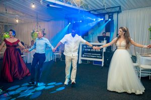 Wedding party dancing in formation on a blue-lit dance floor during reception celebrations.