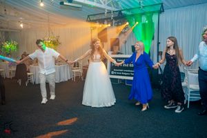 Wedding reception dance floor with guests participating in a group dance under colorful lighting.